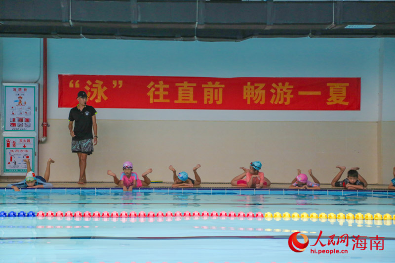 今年暑期，三亞22座泳池暑期向中小學(xué)生免費開放，在三亞市吉陽區(qū)丹州小學(xué)游泳館內(nèi)，教練正指導(dǎo)學(xué)生練習(xí)游泳動作。人民網(wǎng) 牛良玉攝