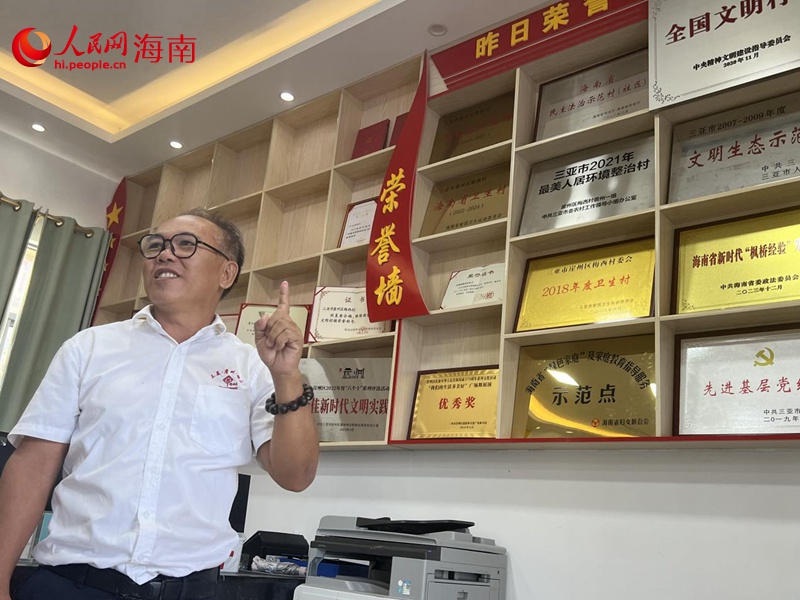 三亞梅西村黨總支書記、村委會主任孫照安向記者介紹榮譽(yù)墻。人民網(wǎng)記者 李學(xué)山攝
